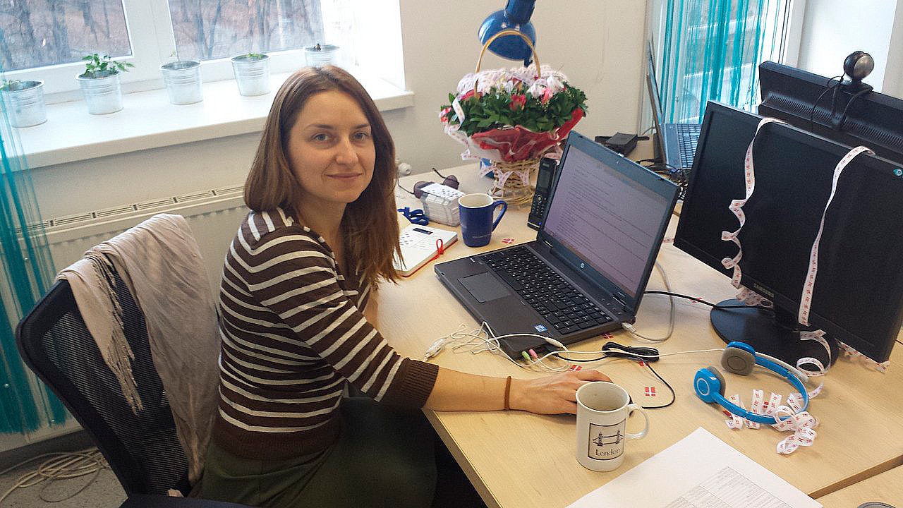 Halyna Shporlyuk sits at her desk on her first day at Conscensia, a Danish flag mug in the foreground and a welcome bouquet, symbolizing the warm reception and the start of her significant journey.