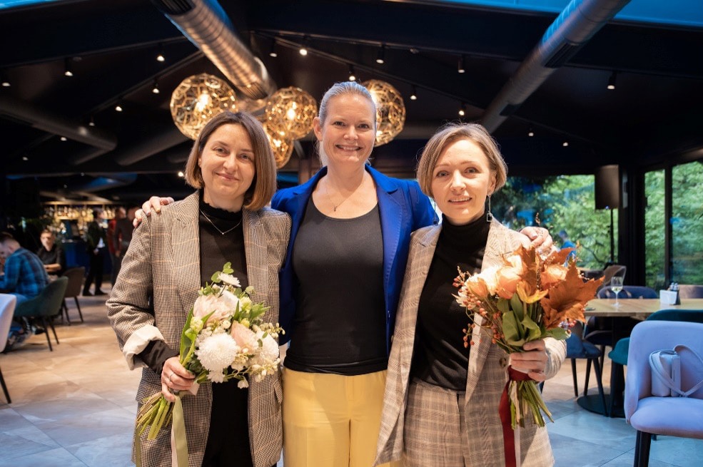 Halyna, Line, and Iryna smiling with flowers at a Conscensia celebration.