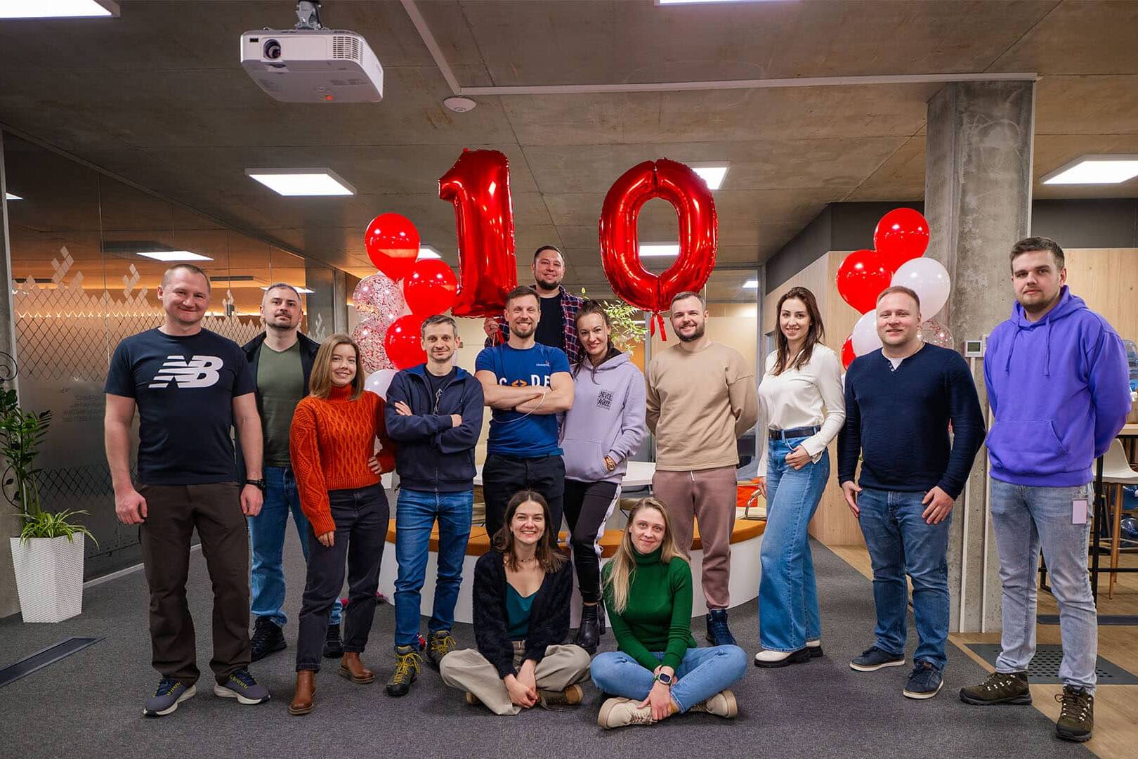 Group of smiling colleagues celebrating 10 years of partnership with red balloons and '10' foil balloons in a Ukraine office