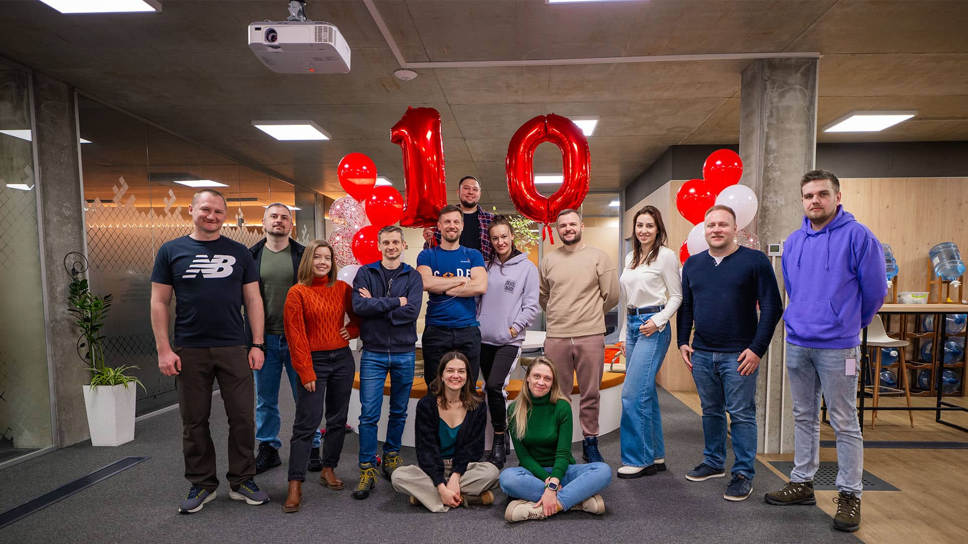 Group of smiling colleagues celebrating 10 years of partnership with red balloons and '10' foil balloons in a Ukraine office