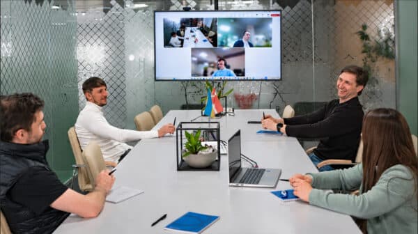 Team members in a meeting room collaborating with remote colleagues on a video call.